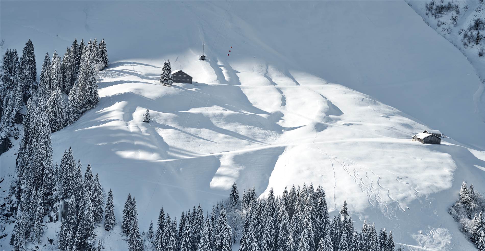 Verschneiter Hang mit Wald und Hütten